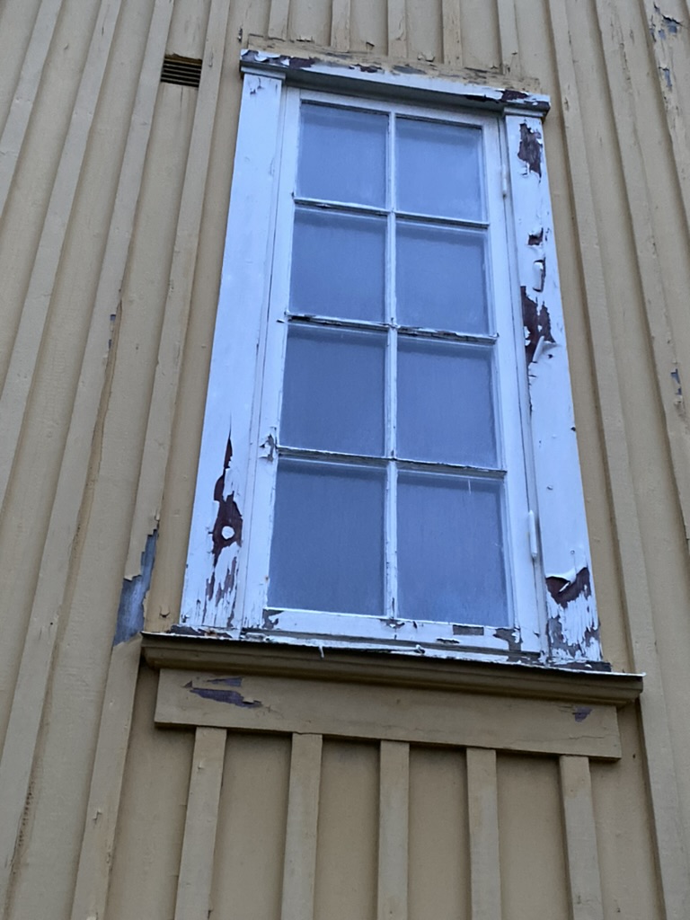 Fönster med kraftigt flagnad färg på gul fasad