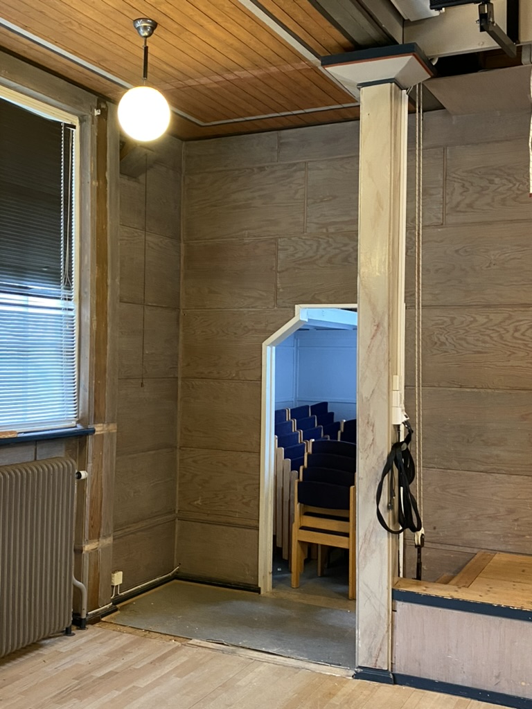 Plywoodväggar och skjutdörr mot rum med blå stolar