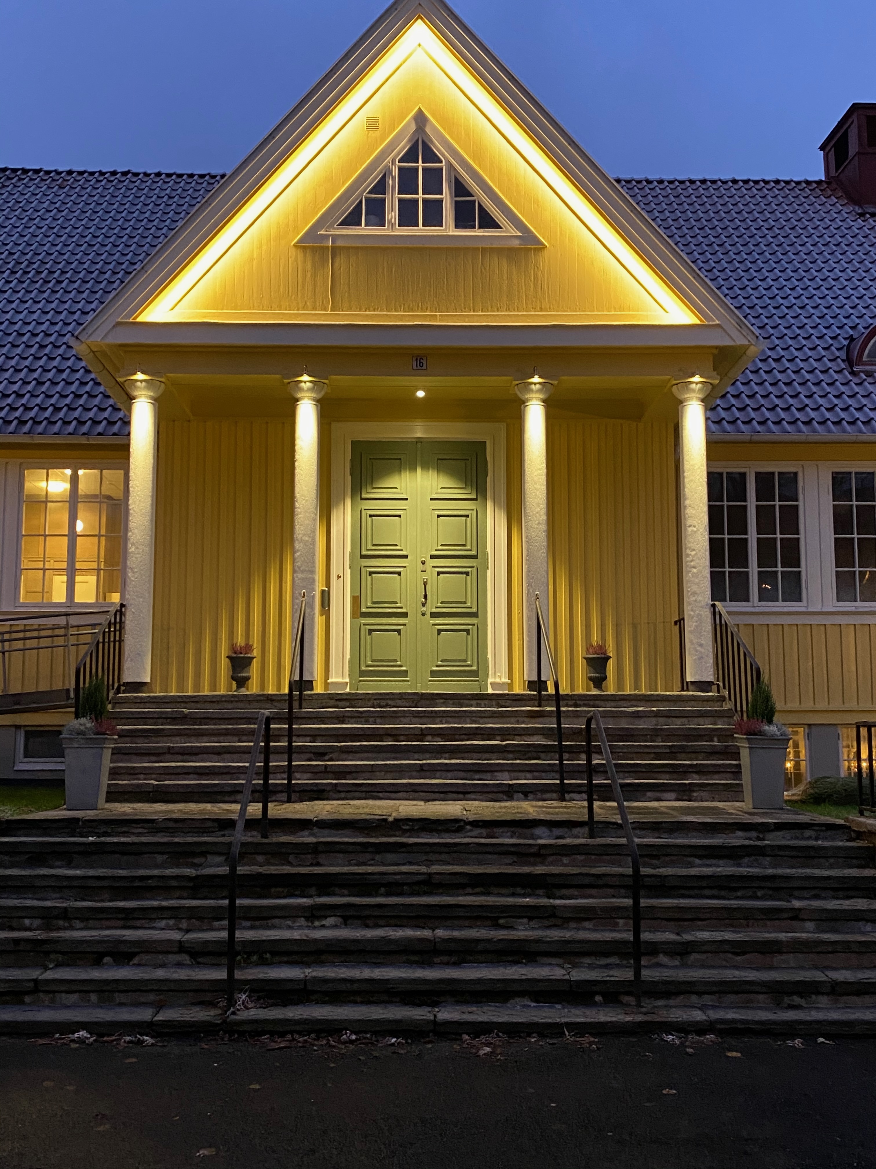 Entrén upplyst på kvällen med varm belysning längs gaveln